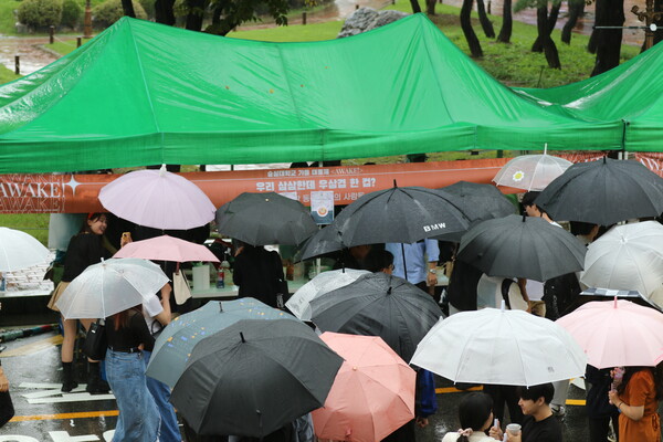 학생들이 우산을 쓰고 주간 부스를 둘러 보고 있다.