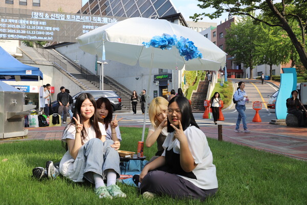 ​학생들이 잔디밭에 앉아 푸드트럭 음식을 먹으며 축제 분위기를 즐기고 있다.​